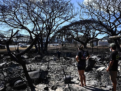Hano Ganer (Rear, C) and Taylor Ganer (Center Right) look through the ashes of their family’s home in the aftermath of a wildfire in Lahaina, western Maui, Hawaii on August 11, 2023