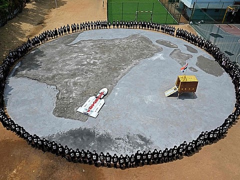 Students with painted faces form a circle around a replica of the Chandrayaan-3 spacecraft in Chennai on August 22, 2023.