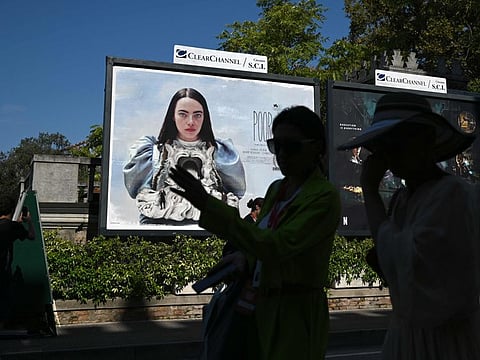 People walk past a poster showing actress Emma Stone on the official poster of the movie 'Poor Things' presented in competition at the 80th Venice Film Festival.