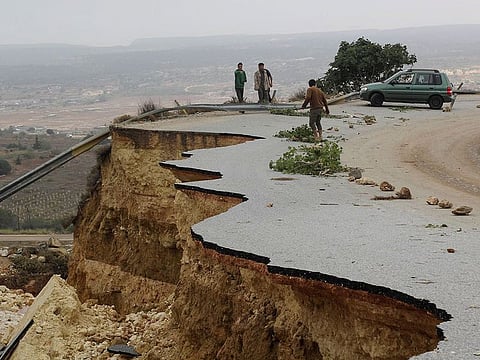 People stand in a damaged road as a powerful storm and heavy rainfall flooded hit Shahhat city, Libya,