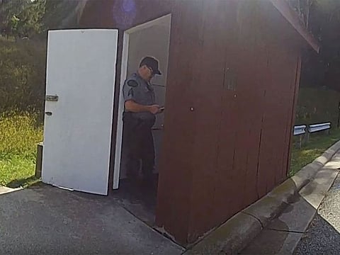 In this photo released by the Michigan State Police, a Department of Natural Resources sergeant stands in the doorway of an outhouse after a woman became trapped in the toilet after attempting to retrieve her Apple Watch, Tuesday, Sept. 19, 2023, at Dixon Lake in Bagley Township, Mich.