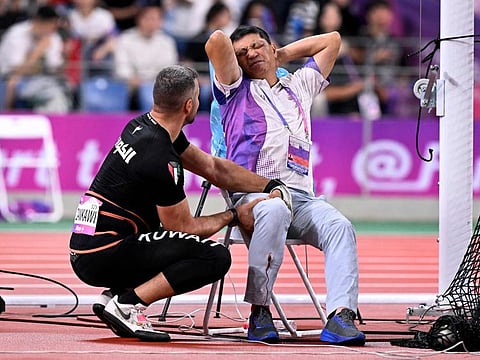 An official reacts in pain after his leg was injured by a stray hammer thrown by Ali Zankawi (left) who attempts to stem the bleeding during the men's hammer throw final athletics event at the Asian Games in Hangzhou on Saturday.