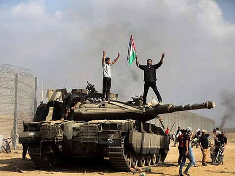 Palestinians wave their national flag and celebrate by a destroyed Israeli tank at the Gaza Strip fence east of Khan Younis southern Saturday, Oct. 7, 2023.