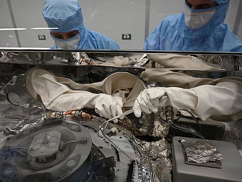 Scientists use tools to collect asteroid particles from the base of a canister.