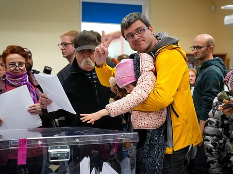 A man flashes a victory sign after casting his ballot with help from a child during parliamentary elections in Warsaw, on Sunday.