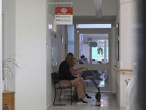 Caroline Wahlberg (L), manager of the Tallhojden nursing home in Sodertalje, sits with an elder man on the bench of a fake bus stop installed in a corridor of the facility dedicated to patients with dementia.