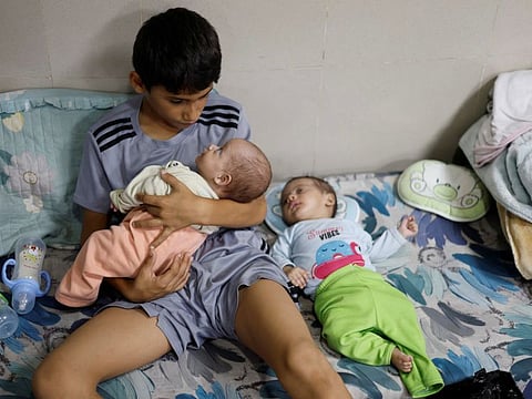A displaced Palestinian boy, who fled with his family from their house amid Israeli strikes, looks after his twin siblings as they take shelter at Nasser hospital in Khan Younis in the southern Gaza Strip October 29, 2023.