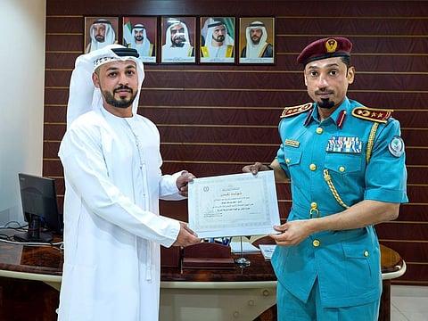 Colonel Dr. Ali Al-Hamoudi, Sharjah Police Director of the Eastern Region Police Department, presents the certificate to Ahmed Youssef Abdullah as a recognition of his commitment to societal well-being and security.