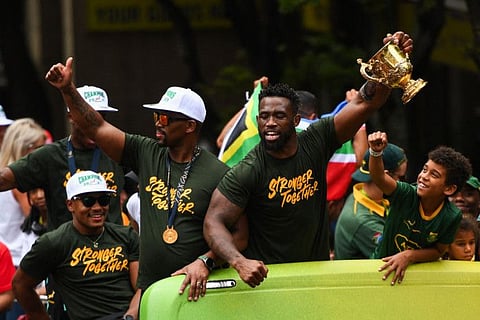 South Africa's flanker and captain Siya Kolisi (right) holds the Web Ellis Cup from a bus, next to assistant coach Mzwandile Stick during the Springboks Champions trophy tour in Cape Town on November 3.