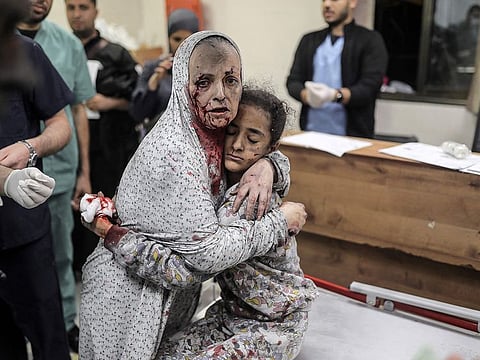 A Palestinian woman covered in dust rushes with her child in her arms into the hospital following the Israeli bombardment of Khan Yunis in the southern Gaza Strip on November 15, 2023