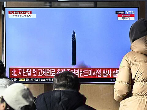 People watch a television screen showing a news broadcast with file footage of a North Korean missile test.