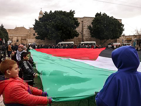 Residents unfurl a giant Palestinian flag as they gather at the Manger Square outside the Church of the Nativity in the biblical city of Bethlehem in the occupied West Bank on Christmas Eve (according to Western tradition) on December 24, 2023.