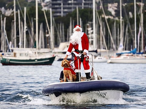 A man dressed as Santa Claus rides a boat with his dog in front of yachts as part of Christmas Day celebrations for the annual Sydney to Hobart yacht race on December 25, 2023.