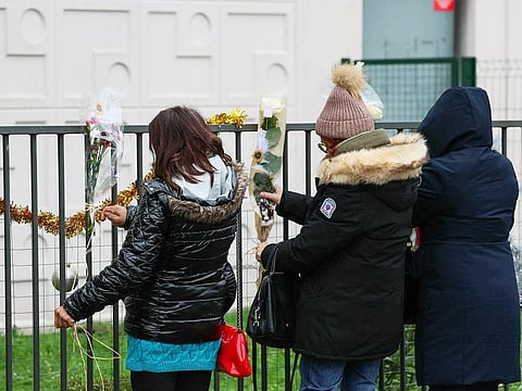 People lay flowers just in front of the ground floor flat where the bodies of a woman and her four children where discovered, in Meaux, eastern Paris, on December 26, 2023.