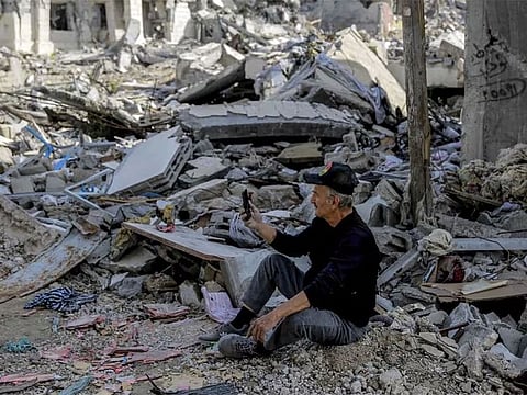 A Palestinian man uses his phone as he sits amid the rubble of destroyed buildings in Gaza City. Thanks to embedded SIM cards, Palestinians can still access the internet and maintain a channel of communication with loved ones abroad.