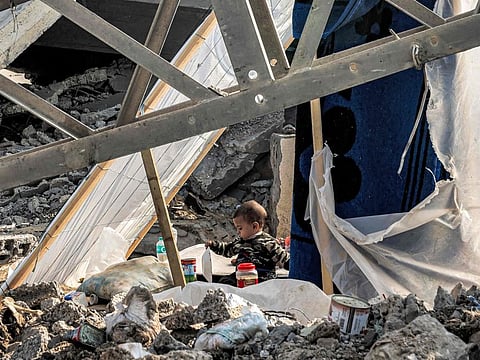 A child holds a plate while sitting between rubble in Rafah in the southern Gaza Strip on January 2, 2024.