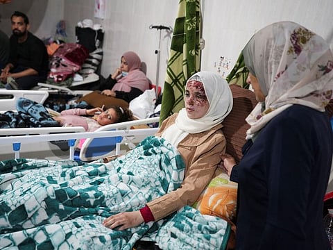 Palestinians wounded in Israeli strikes lie on beds as displaced people shelter at Shuhada Al-Aqsa Hospital.