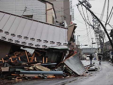 People walk past a damaged building in the city of Suzu, Ishikawa prefecture.