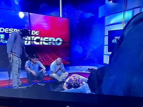 Workers lie on the floor as hooded and armed people take over a tv studio of Ecuador's TV station TC during a live broadcast.
