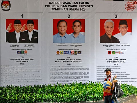 A street vendor carrying his belonging walks past a banner showing presidential candidates contesting the upcoming general election in Jakarta, Indonesia, January 12, 2024