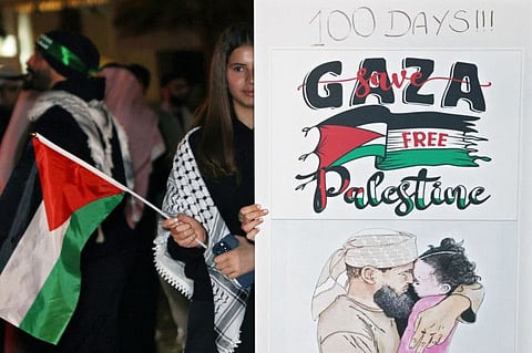 A Kuwaiti woman wearing the traditional Palestinian keffiyeh waves a Palestinian flag as she stands behind a placard during a rally in solidarity with the people of Gaza at Iradah Square in Kuwait City on January 14, 2024.