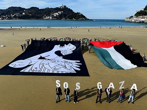 Demonstrators hold a canvas with a detail of Spanish painter Pablo Picasso's masterpiece "Guernica" depicting a mother, and wave a giant Palestinian flag during a protest in solidarity with the Palestinian people under the slogan "SOS Gaza", on La Concha beach in the Spanish Basque city of San Sebastian on January 28, 2024.