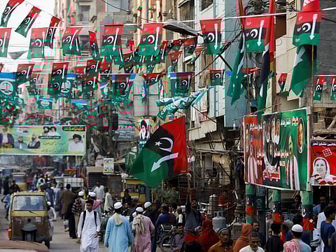 People walk along a street decorated with campaign flags and posters of political parties, ahead of general elections, in Karachi.