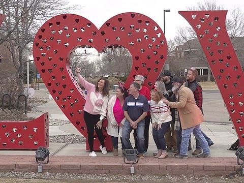 Volunteers pose for a photo in front of a “Love” art installation at the visitors center in Loveland, on February 7, 2024.