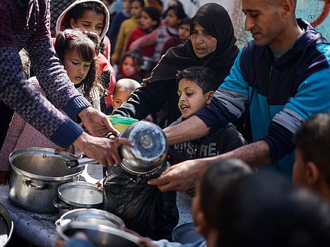 Palestinian children wait to receive food cooked by a charity kitchen amid shortages of food supplies