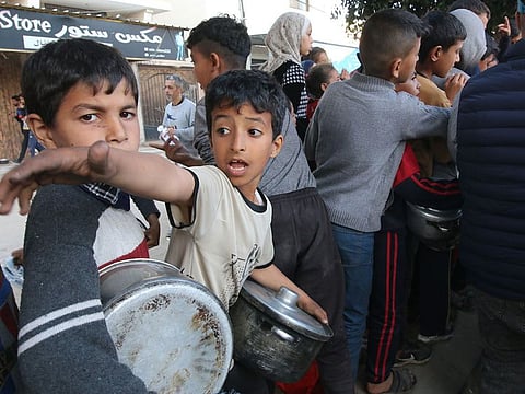 Displaced Palestinian children wait to collect free food handouts from a street kitchen in Deir Al Balah, central Gaza