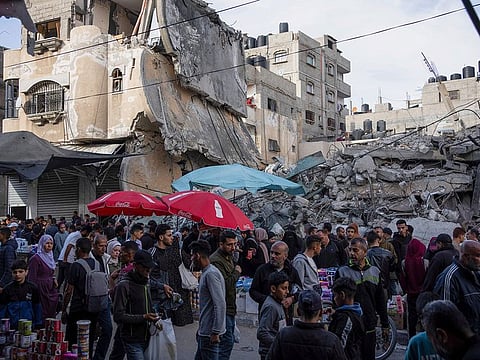 Palestinians buy food at a local market next to a destroyed residential building by the Israeli airstrikes, during the month of Ramadan, in Rafah, Gaza Strip, Thursday, March 14, 2024.