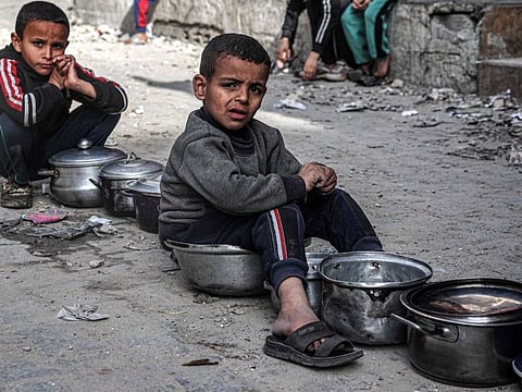 Boys sit with empty pots as displaced Palestinians queue for meals provided by a charity organisation ahead of an iftar meal in Rafah in the southern Gaza Strip on March 16, 2024.