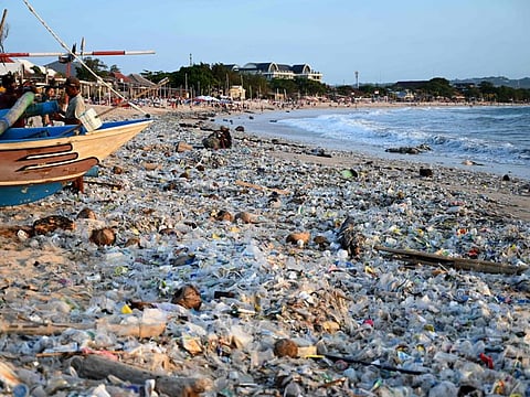 A man (C) collects recyclable items to sell amid plastic and other debris washed ashore at Kedonganan Beach near Denpasar on Indonesia's resort island of Bali on March 19, 2024. (Photo by SONNY TUMBELAKA / AFP)