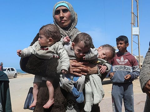 A Palestinian woman fleeing Al Shifa hospital following an Israeli raid, carries her triplet children as she moves southward, amid the ongoing conflict between Israel and Hamas, in the central Gaza Strip on March 21, 2024.