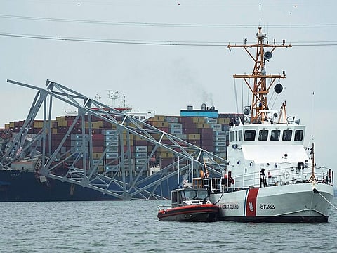 A Coast Gaurd cutter patrols in front of a cargo ship that is stuck under the part of the structure of the Francis Scott Key Bridge after the ship hit the bridge.