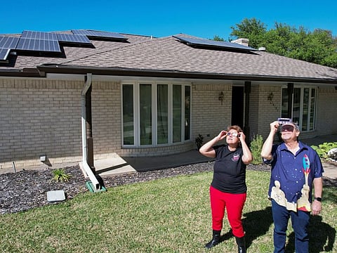 Eclipse chaser Leticia Ferrer and her husband Daniel Brookshier observe the sun through eclipse glasses, in front of their home in Dallas, US, on April 3, 2024.