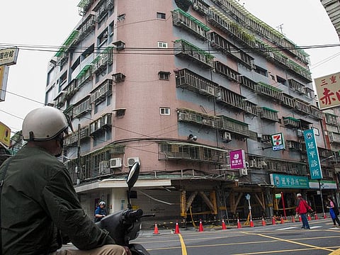 A motorcyclist looks at a tilted building caused by the April 3 magnitude-7.4 earthquake at Tucheng district in New Taipei City on April 6, 2024.