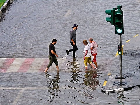 Pedestrians cross the road at a half-submerged zebra crossing in Sharjah’s Al Majaz after heavy rain on April 16, 2024.