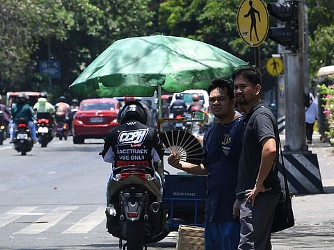 A pedestrian cools himself with a folding hand fan as he waits for a ride along a road in Manila on April 24, 2024.