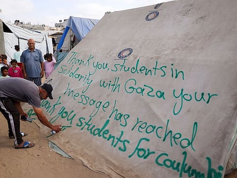 A man writes a message of thanks to students in the US protesting in solidarity with the people of Gaza, on a tent at a camp for displaced Palestinians in Rafah, in the southern Gaza Strip on April 27, 2024.