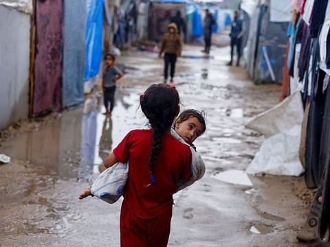 A displaced Palestinian girl holds a child as she walks at a tent camp on a rainy day in Rafah, in the southern Gaza Strip, on May 6, 2024.