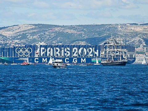 The French 19th-century three-masted barque Belem sailing in front of the Greenland container ship of the CMA CGM with containers with the logo of Paris 2024 Olympic Games in the bay of Marseille, in the Mediterranean Sea, on Wednesday.