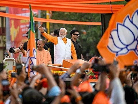 Narendra Modi , India's Prime Minister and leader of the ruling Bharatiya Janata Party (BJP) with Yogi Adityanath, Chief Minister of the country's Uttar Pradesh state waves to the crowd during his roadshow on the eve of filing of his election nomination papers, in Varanasi on May 13, 2024.