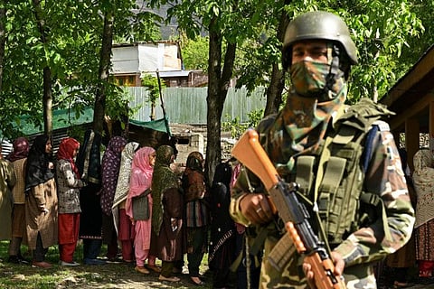 A security personnel stands guard as voters queue up to cast their ballots at a polling station during the fourth phase of voting in Indias general election, in Ganderbal district, northeast of Srinagar on May 13, 2024.