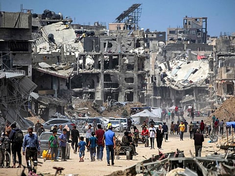 People move past destroyed buildings along a street in Khan Younis in the southern Gaza Strip on May 14, 2024.