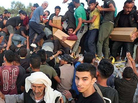 Palestinians climb on a truck to grab aid that was delivered into Gaza through a US-built pier, amid the ongoing conflict between Israel and the Palestinian Islamist group Hamas, as seen from central Gaza Strip, May 18, 2024.