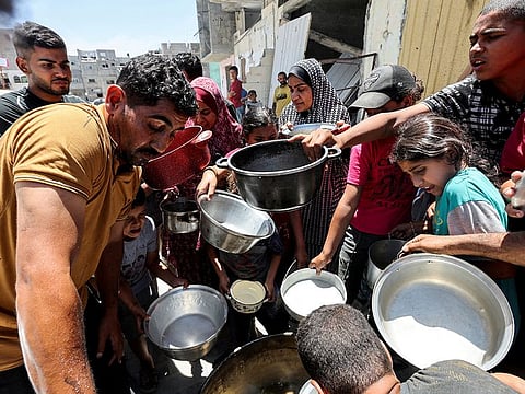 Palestinians gather to receive food cooked by a charity kitchen near houses destroyed in the Israeli military offensive, in Khan Younis in the southern Gaza Strip, May 30, 2024.