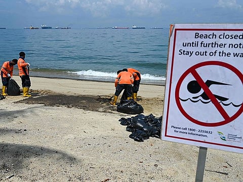 Workers clear the oil slick in plastic bags on Sentosa island's Tanjong Beach in Singapore on June 16, 2024. Beaches on Singapore's top resort island of Sentosa, which also house luxury waterfront homes, were shuttered on June 15 due to an oil spill at a nearby port, maritime authorities said
