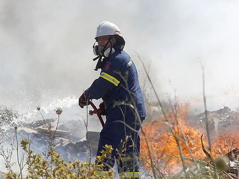 A firefighter uses a hose as he attempts to extinguish flames after a wildfire broke out in Kitsi, a southern suburb of Athens.