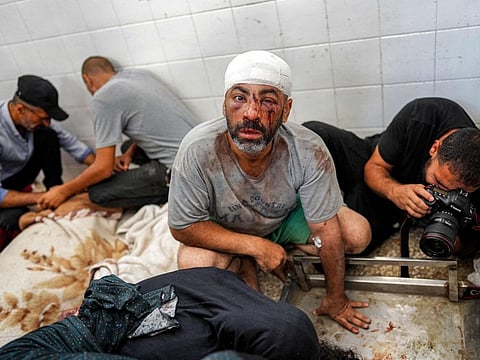 An injured man looks on as behind him a photojournalist documents the scene at a morgue holding the bodies of people killed in the aftermath of overnight Israeli bombardment in Al Maghazi in the central Gaza Strip, at Al Aqsa Martyrs hospital in Deir Al Balah on June 25, 2024.